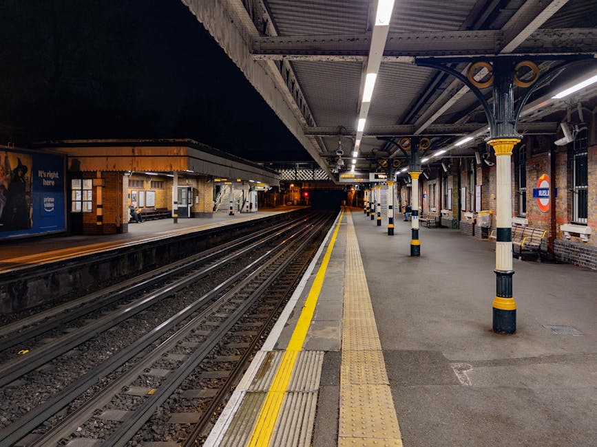 At Kennington station's underground entrance, four individuals are engaged in conversation. An elderly man stands near a blue recycling bin, holding a green plastic bag, while a young man with a backp